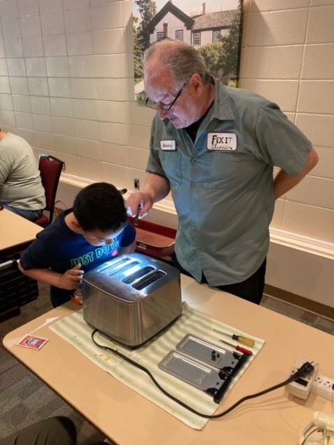 Image of Fixit Clinic Volunteer fixer showing young boy how to repair a toaster