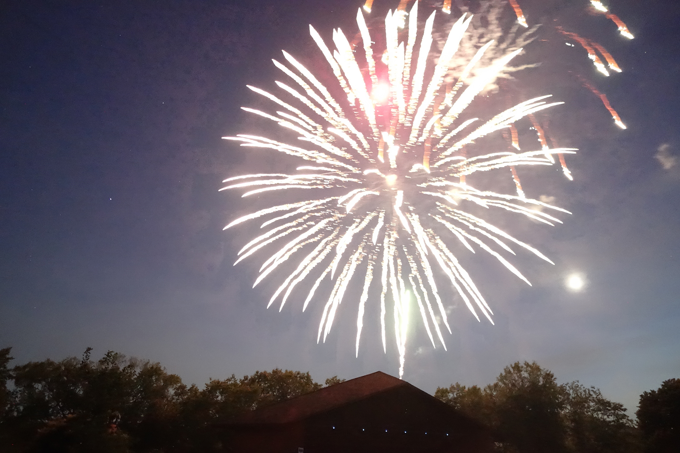 Large firework exploding over the Normandale Lake Bandshell with a streaking tail below during Summer Fete 2022