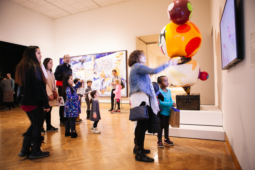 Visitors of varying ages view video in Mia gallery next to large sculpture.