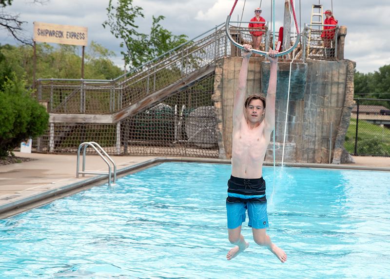 Swimmer riding zip line above pool